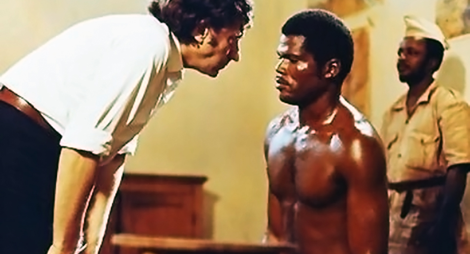A man in a white shirt leans over a shirtless prisoner in Sarah Maldoror's 1972 film Sambizanga.