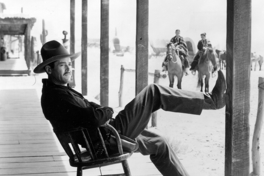 Henry Fonda as Wyatt Earp sits on a wooden porch with his leg on a column in a shot from My Darling Clementine