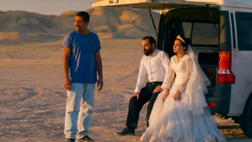 A man in t-shirt and jeans stands next to a bride and groom in a scene from It Was Just an Accident (2025).