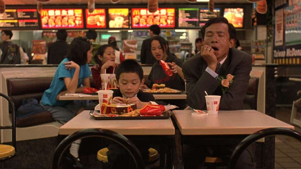 A young boy and his yawning father eat at a Taiwan McDonald's while wearing wedding suits in a shot from Edward Yang's Yi Yi (2000)