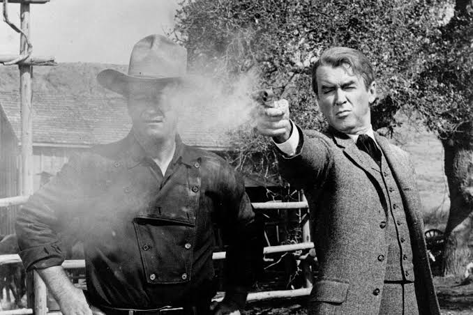 Jimmy Stewart fires a gun while standing next to John Wayne in a scene from The Man Who Liberty Valance (1962).